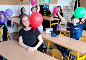 Uczniowie w ławkach z balonami.